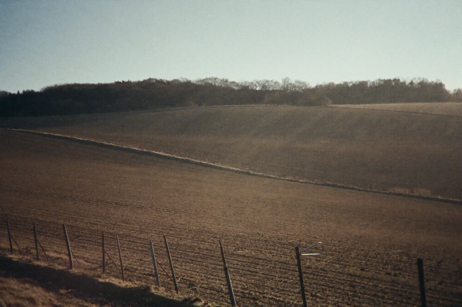 Rolling farmland under low winter light, fence line running along the field edge