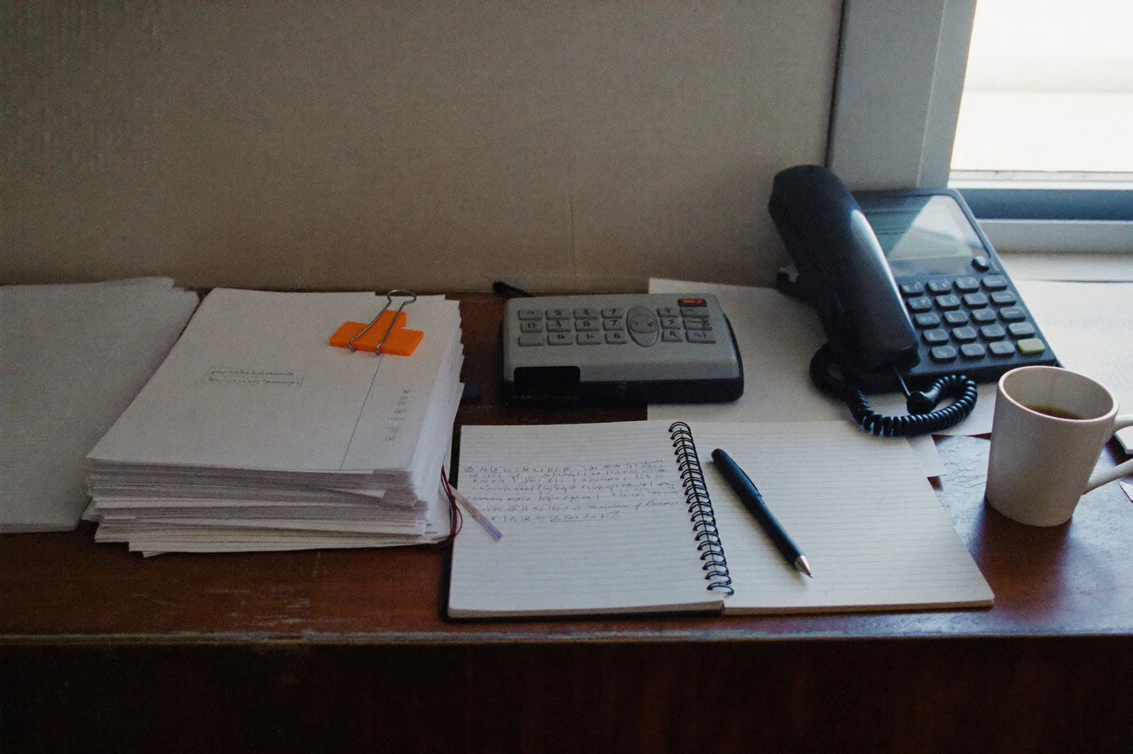 The back counter of a small business: a stack of invoices, a card reader, a notebook and a cooling coffee