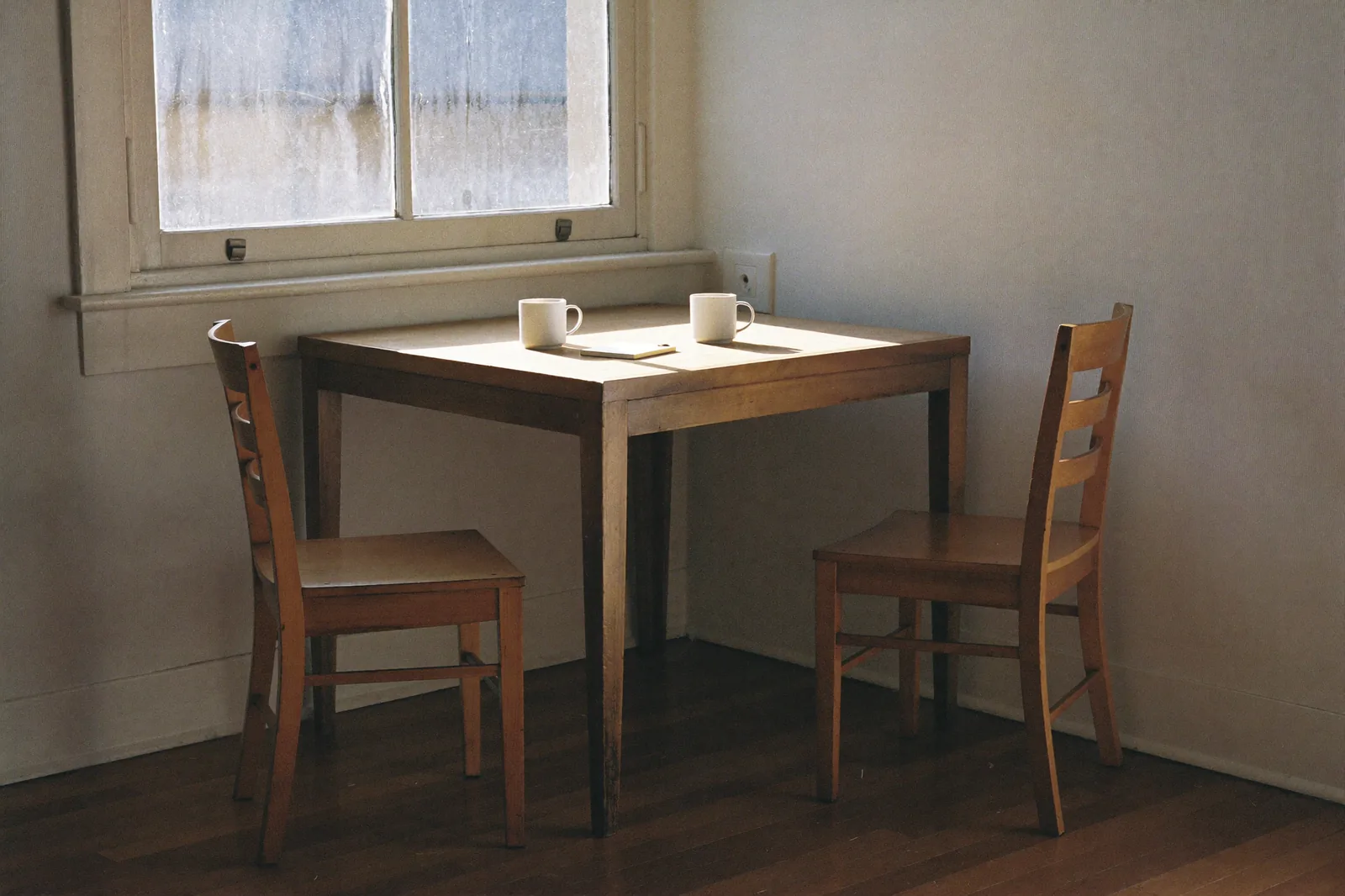 Two chairs at a table by a window, set for a conversation