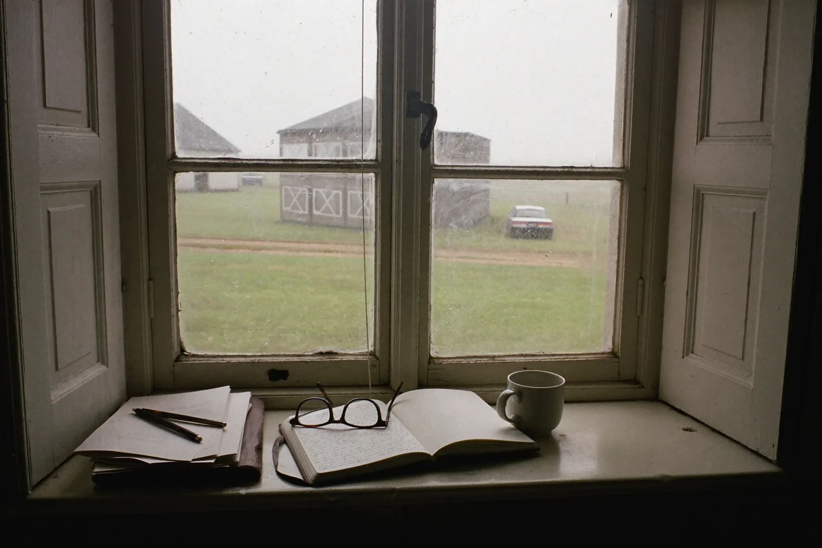An open notebook and reading glasses on a deep windowsill, looking out over a field